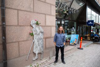 Taiteilija Sami Leutola teoksensa vieressä. Teos on teräksinen mummo, jolla on kävelykeppi.