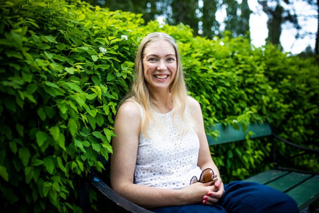 Henkilö istuu penkillä vihreän puskan edessä.