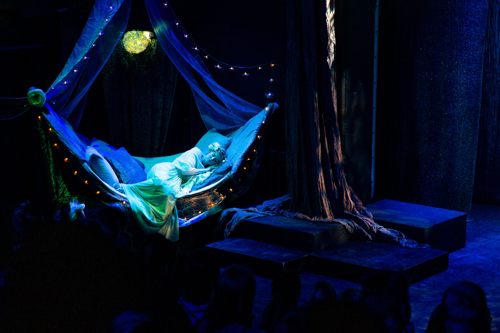 Hämärällä näyttämöllä nuori nainen lepäilee satumaisessa sängyssään