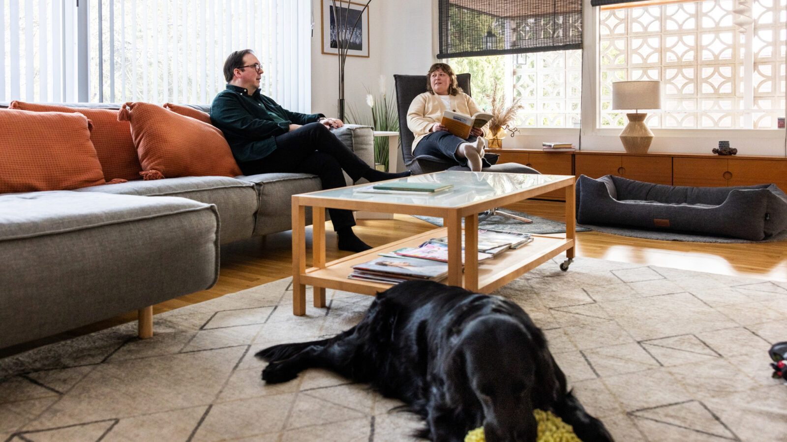 Pariskunta istuu kotonaan sohvalla ja koira makoilee kuvan edustalla lattialla.