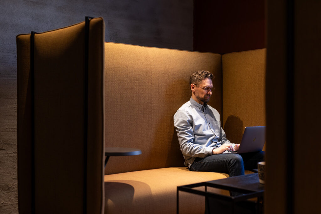 Mies istuu korkeanojaisessa tuolissa tietokoneen äärellä työskentelemässä.