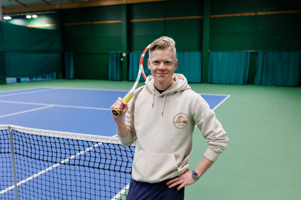 Harri Reiman seisoo tenniskentän laidalla ja pitää tennismailaa olallaan.