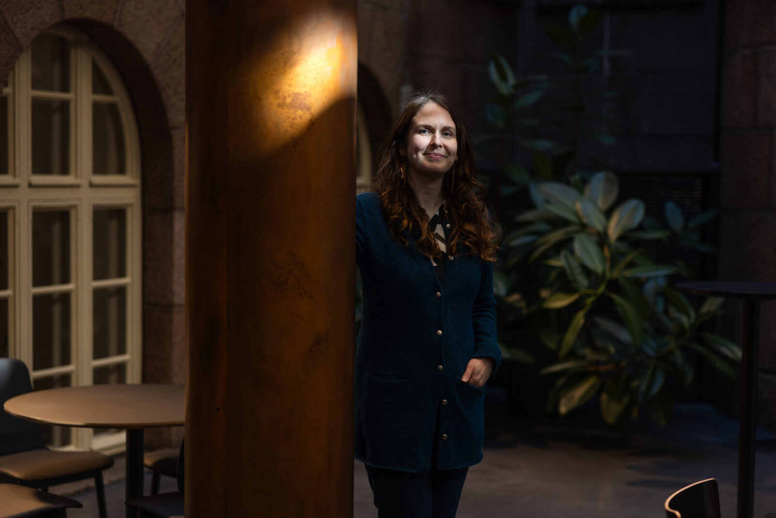 Jenni Rahkonen poseeraa kameralle, Hän seisoo vasen käsi puseron taskussa, oikea käsi on pylvään takana.