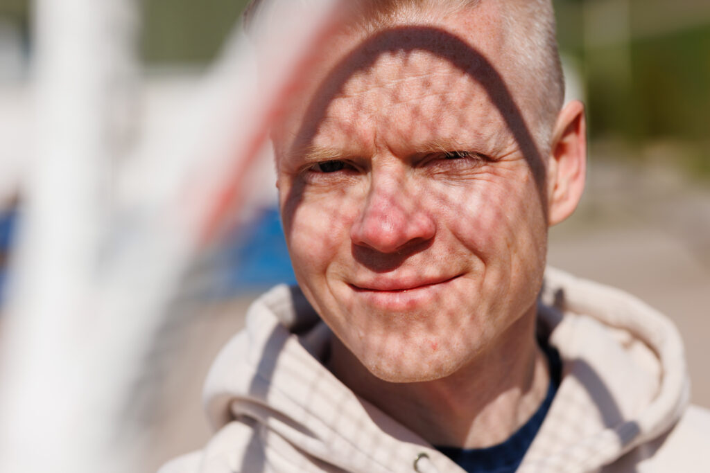 Harri Reiman lähikuvassa. Aurinko paistaa miehen kasvoille johon heijastuu myös tennismailan verkkokuvio.