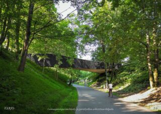 Havainnekuvassa tummasävyinen kaareva silta ylittää Loviisanpässin vanhan ratauoman, mikä on nykyään suosittu jalankulun ja pyöräilyn väylä keskustaan Vesijärvenkadun kupeessa.