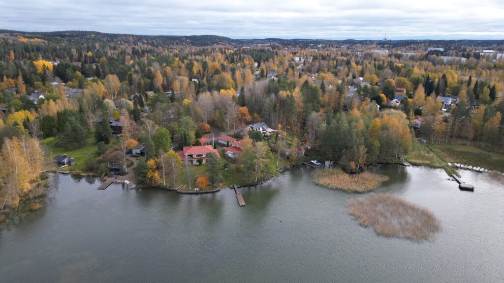 Ilmakuvassa etualalla järveä ja taaempana omakotitaloaluetta metsäisissä maisemissa.