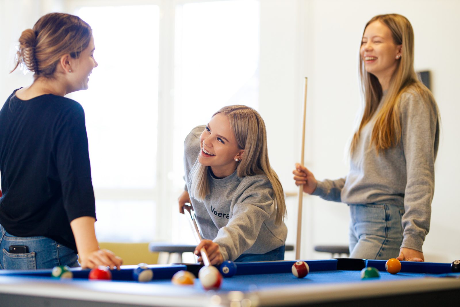 Kolme lukiolaista pelaamassa biljardia.