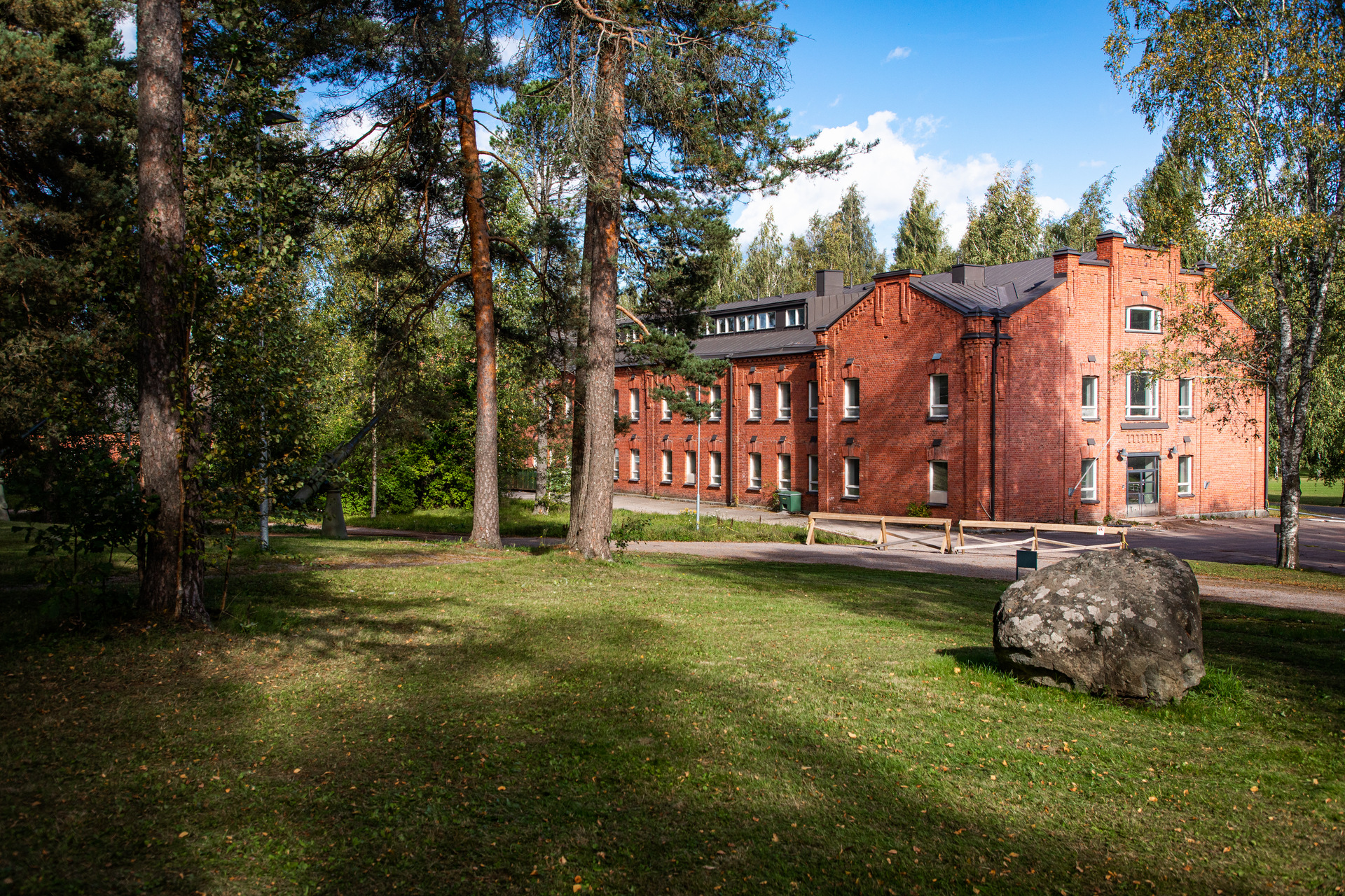 Punatiilinen kasarmirakennus puiden varjossa.