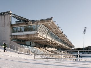 Hiihtäjä urheilukeskuksen stadionrakennuksen vieressä.