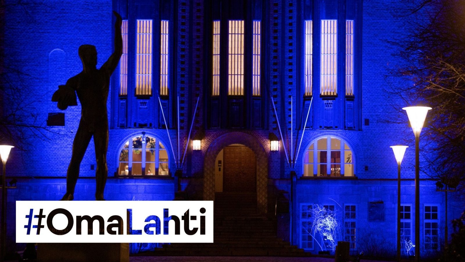 Kaupungintalo sinisessä valaistuksessa ja etualalla teksti #OmaLahti.
