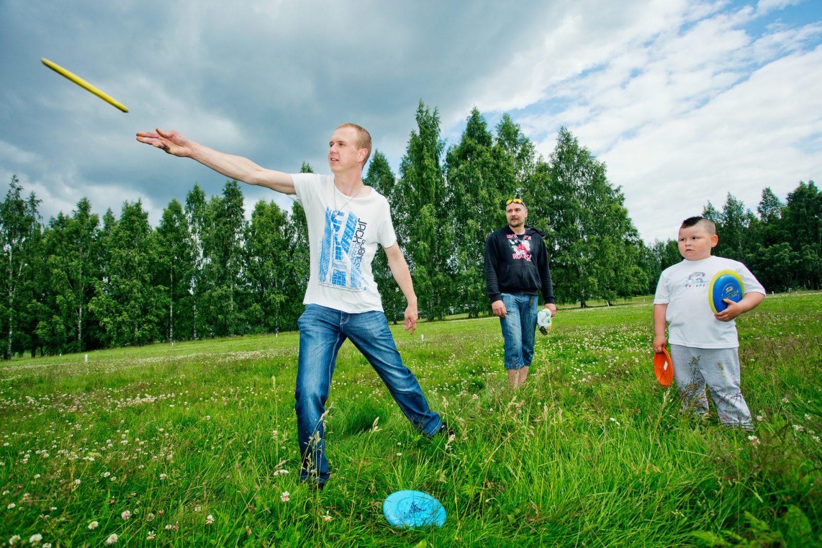 Kolme ihmistä pelaamassa frisbeegolffia nurmiaukealla kesällä