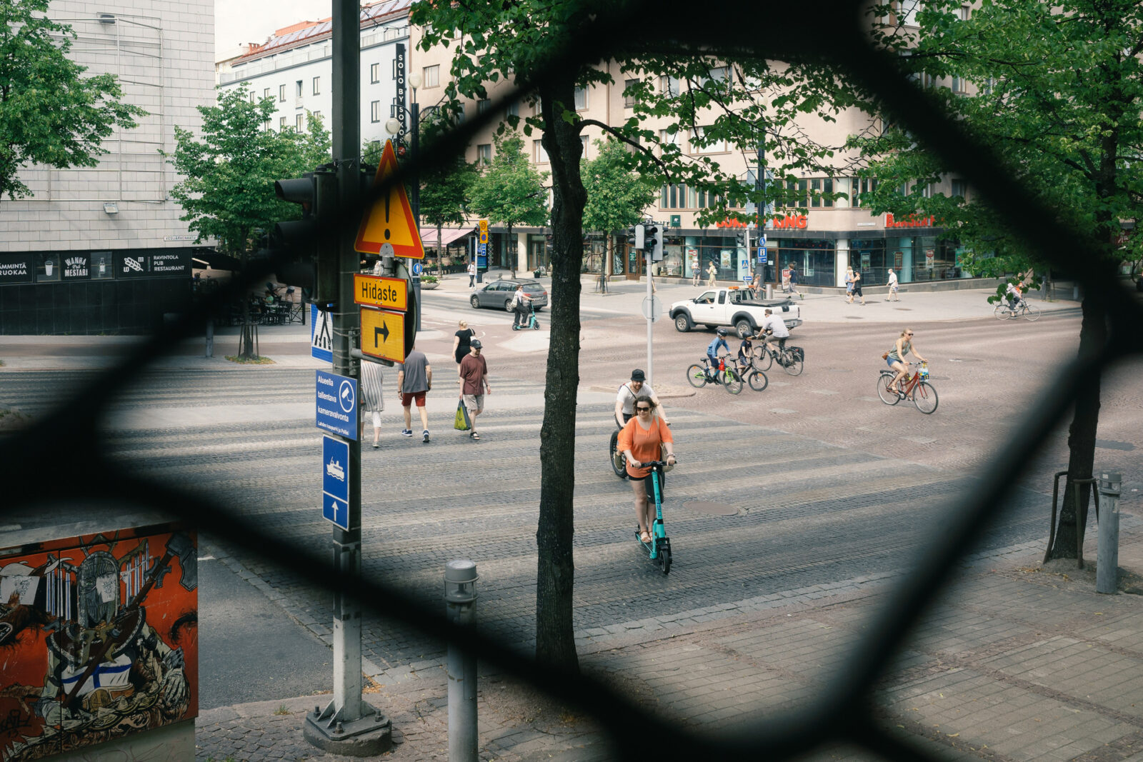 Verkon raosta näkyy suojatietä ylittämässä jalankulkijoita, pyöräilijöitä ja sähköpotkulaudalla kulkevia