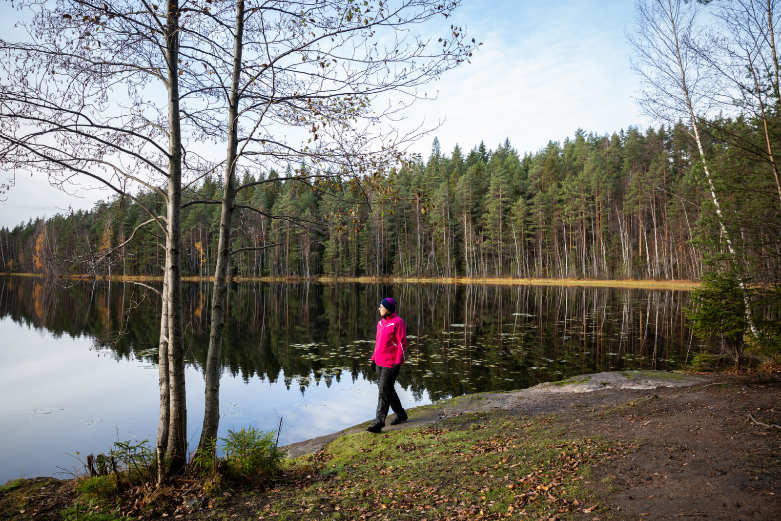 Punatakkinen nainen kävelee luontopolulla. Takana näkyy syksyinen Turranlammi.