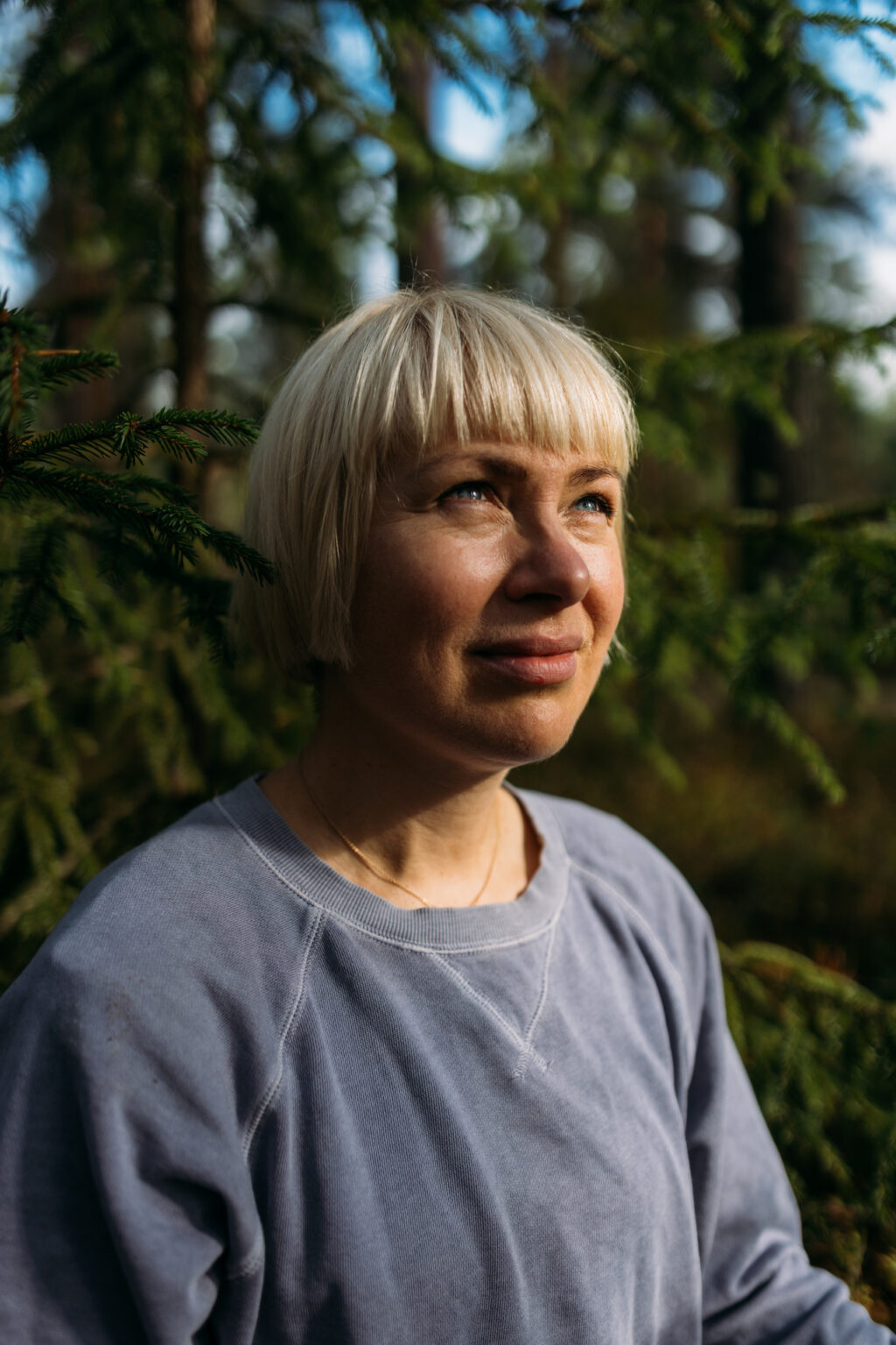 Vaaleahiuksinen nainen katsoo yläviistoon metsässä.