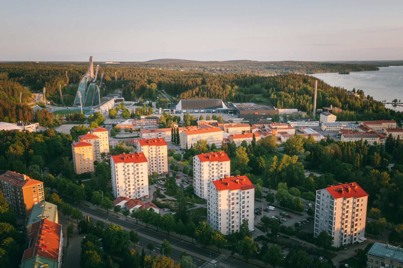 Ilmakuva Lahdesta, jossa näkyy auringonlaskussa kerrostaloja ja taustalla hyppyrimäki.