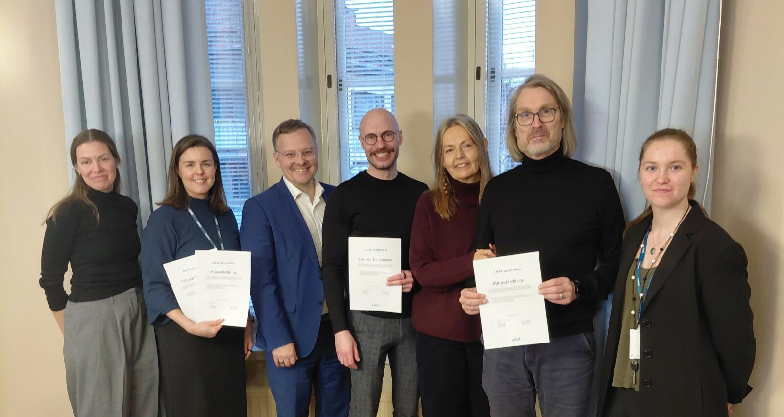 Kuvassa on 7 henkilöä, jotka poseeraavat rivissä hymyillen. Kolmella henkilöistä on allekirjoitetu ilmastokumppanuussopimus kädessään.